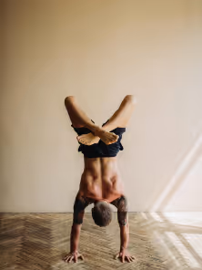 Person performing a handstand on a wooden floor near a sunlit wall.