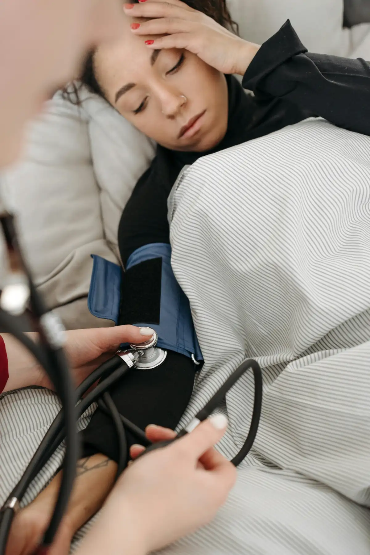 Woman resting in bed having her blood pressure measured with a cuff by a healthcare professional.