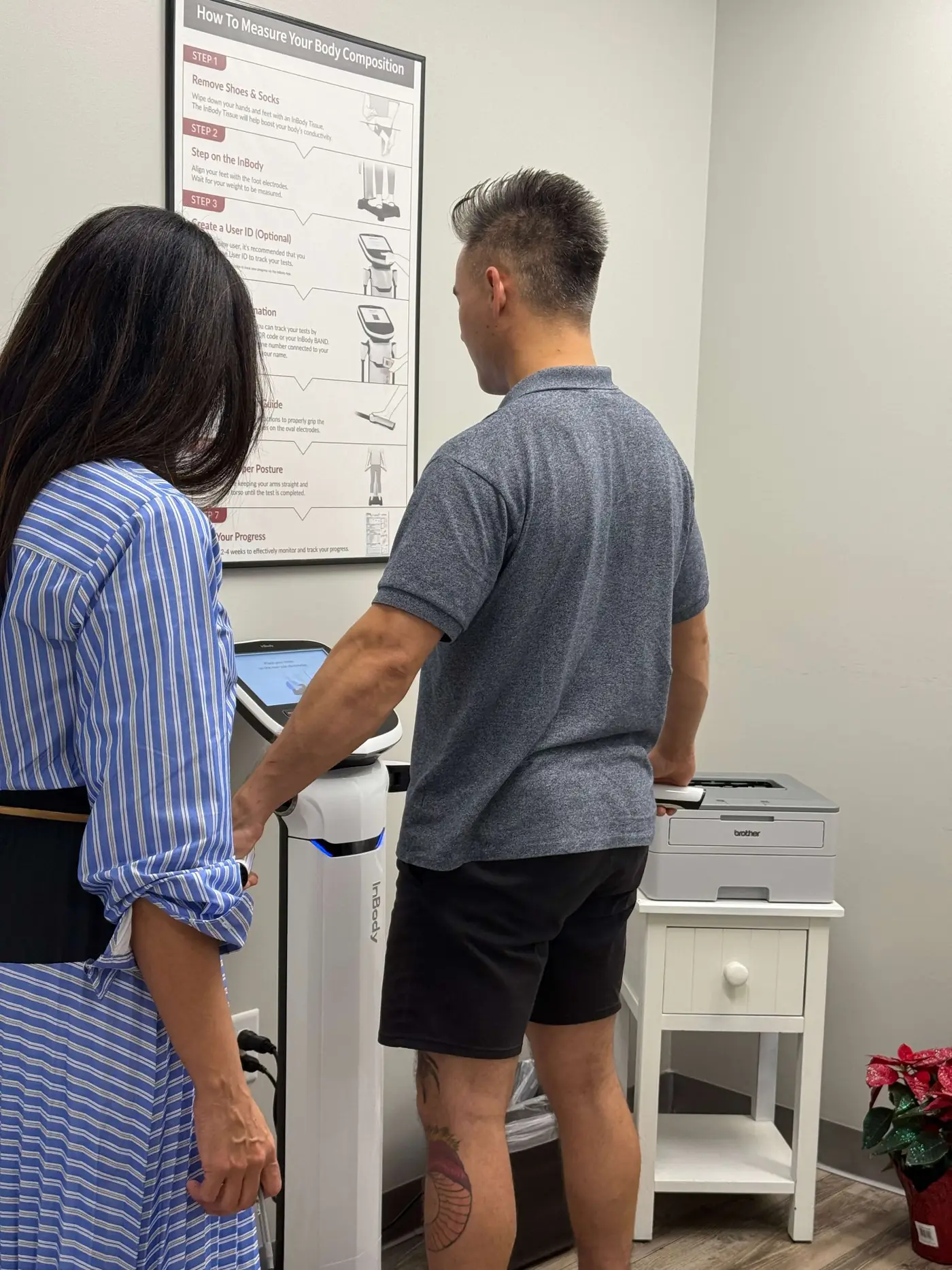 Man using an InBody body composition analyzer while a woman in a blue striped dress observes.