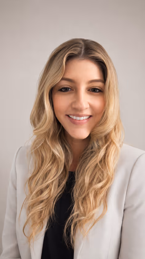 Smiling woman with long blonde wavy hair wearing a light blazer and black top against a plain background.