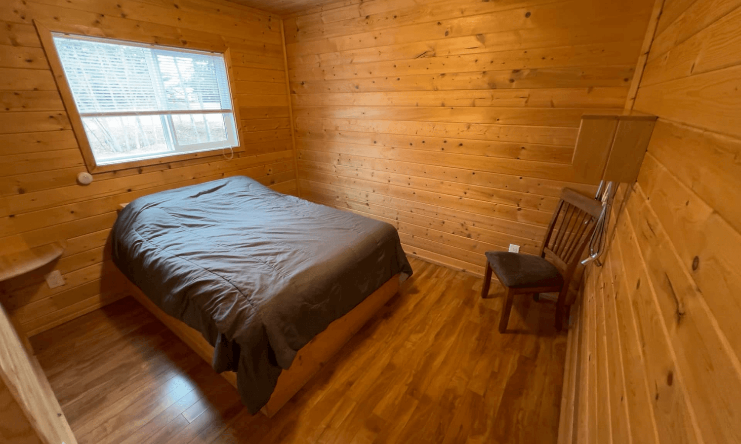 Private cabin bedroom with wooden walls, made bed, and window