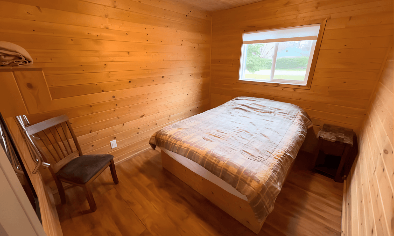 Small cabin bedroom with made bed, wicker accent chair, and window