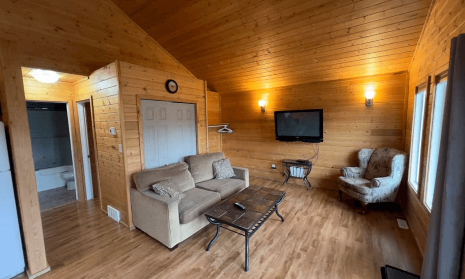 Open cabin living room with sofa, armchair, wall-mounted TV, and wood ceiling