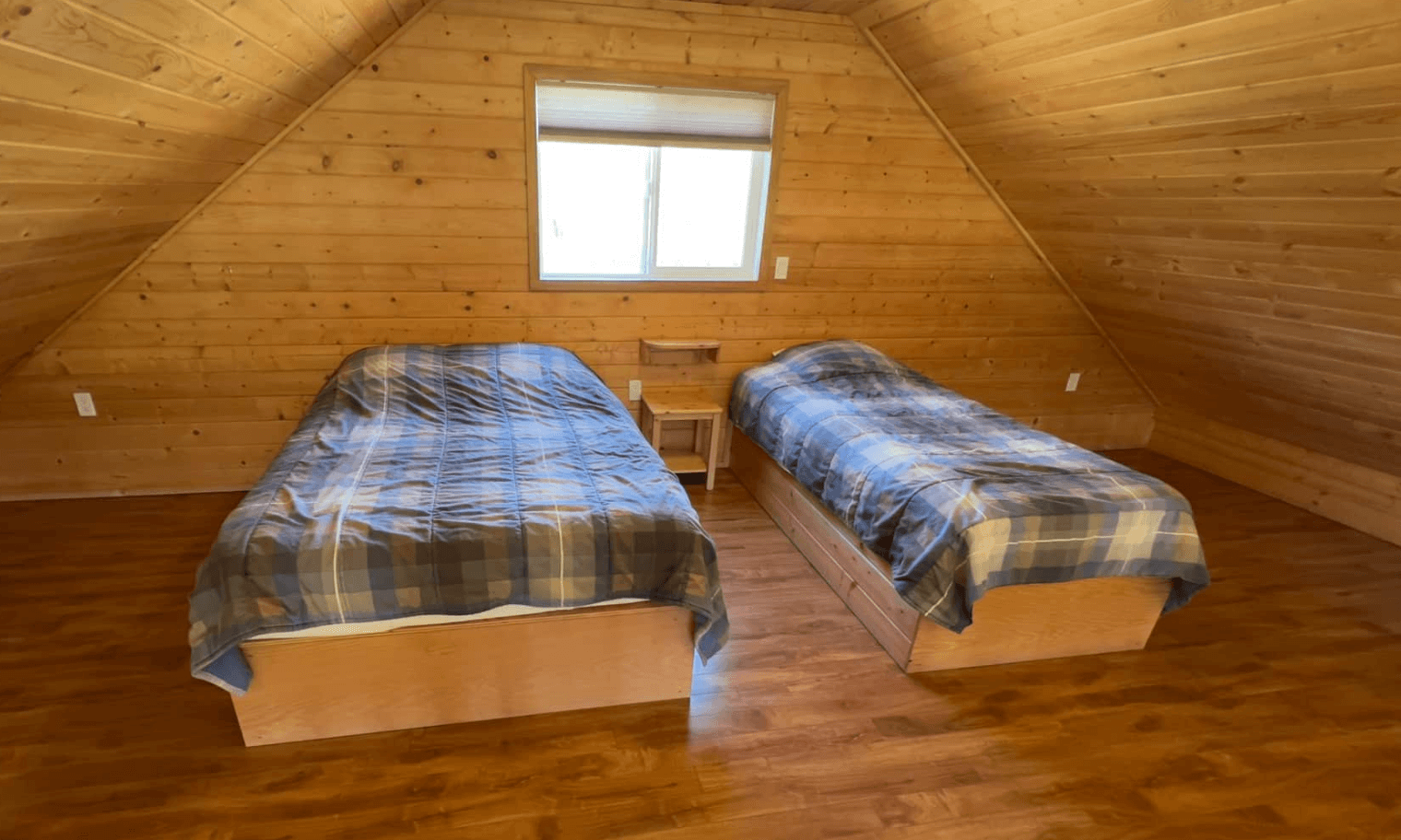 Cozy attic bedroom with two single beds and wood paneling.