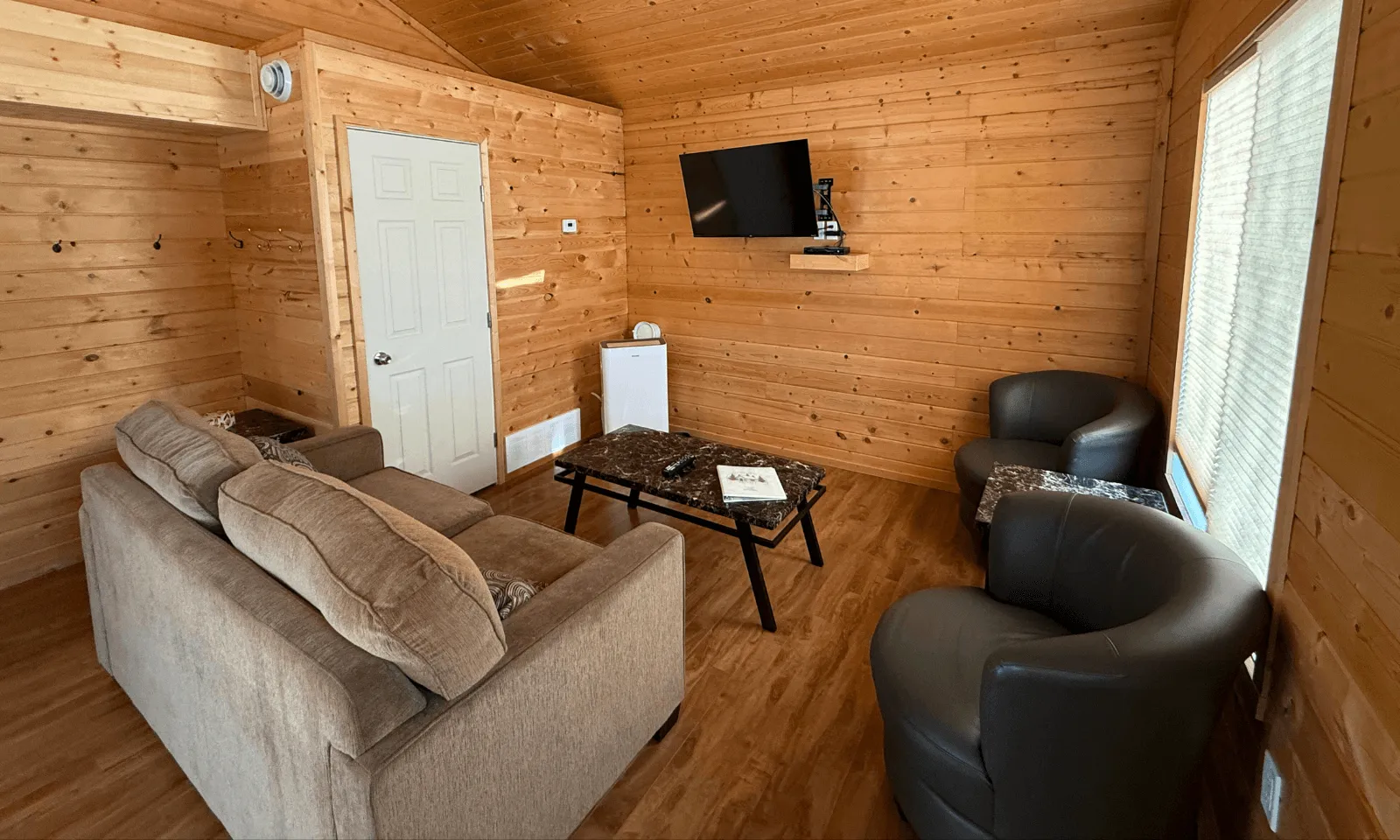 Cozy wood-paneled room with a bed, a black leather chair, a small desk, and a window.