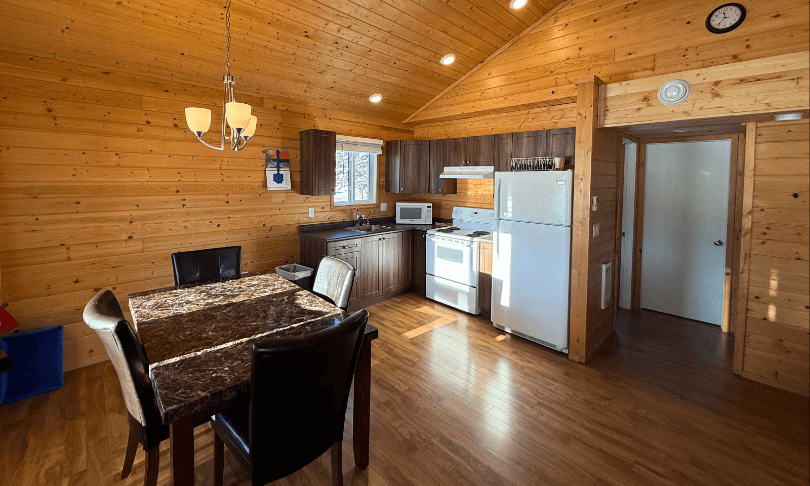 Cozy wood-paneled cabin interior with a dining table, chairs, and a compact kitchen area in the background.