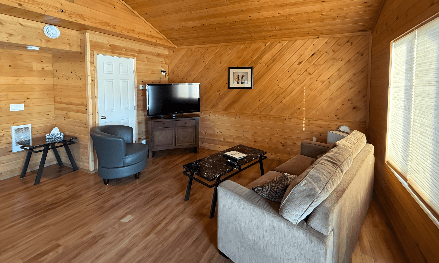 Cozy wood-paneled living area with a sofa, armchairs, coffee table, and a TV.