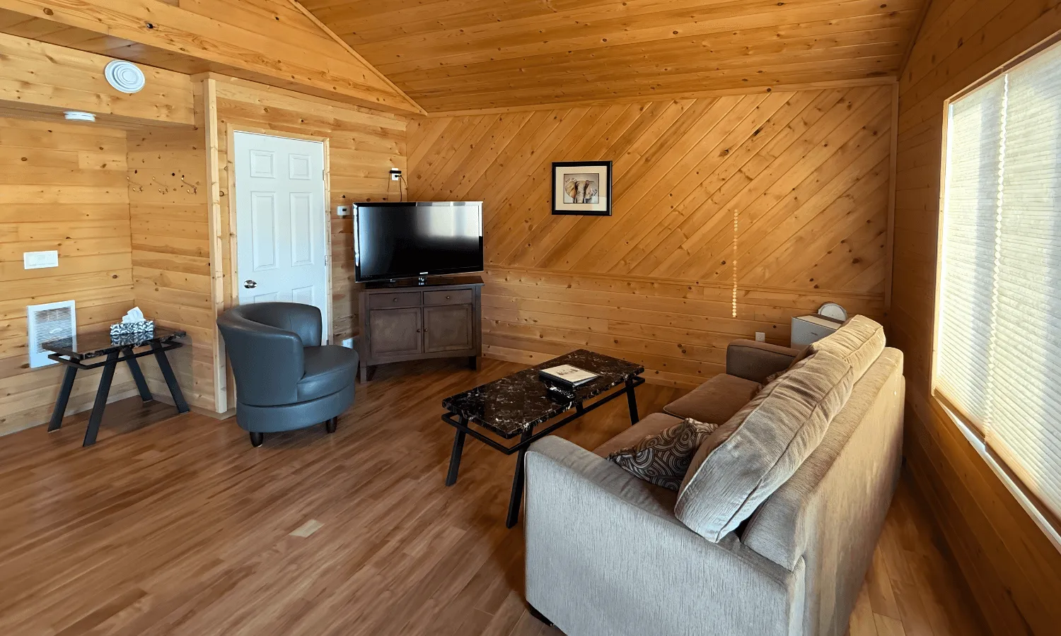 Cozy wood-paneled living area with a sofa, armchairs, coffee table, and a TV.