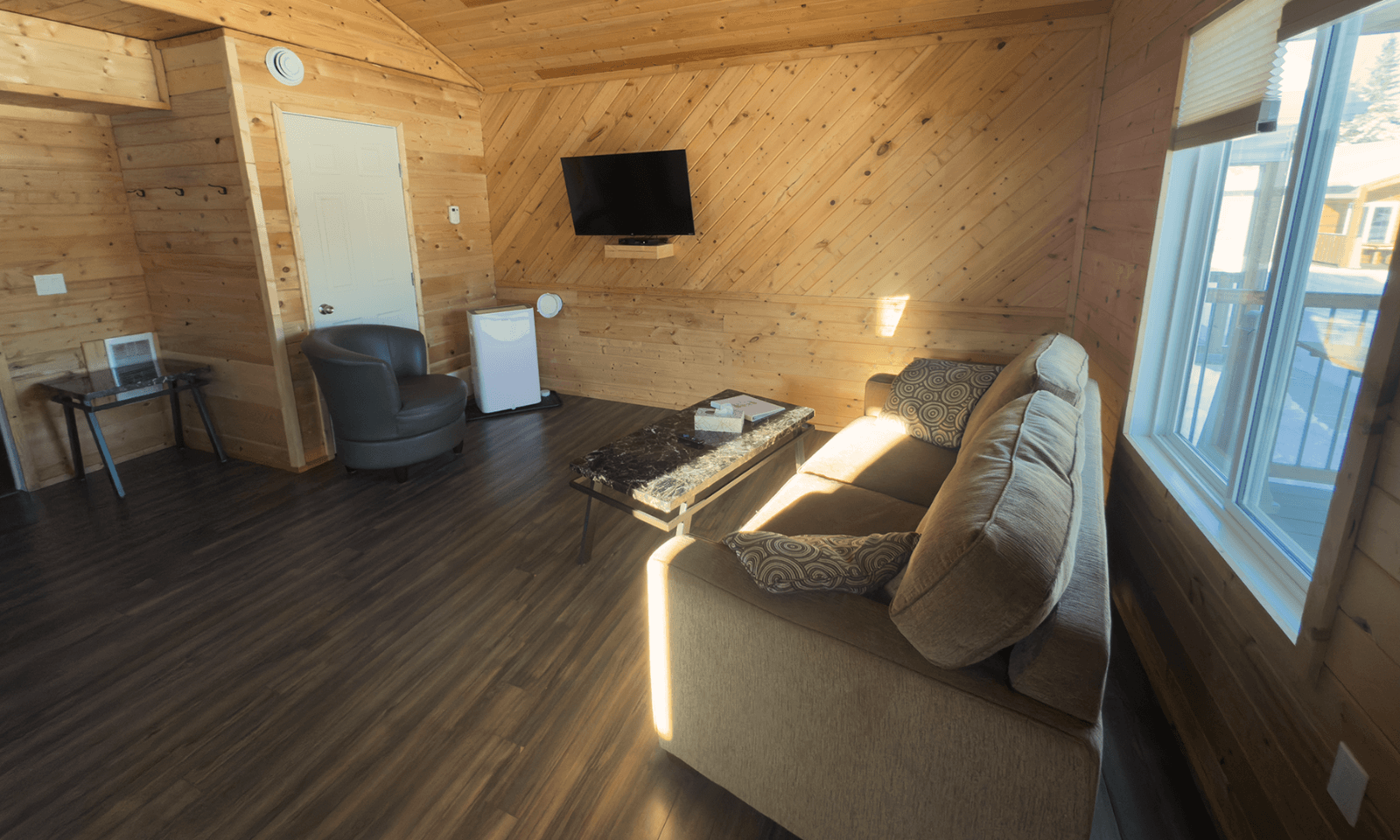 living room with wood-paneled walls, gray sofa, armchair, wall-mounted TV, and large window.