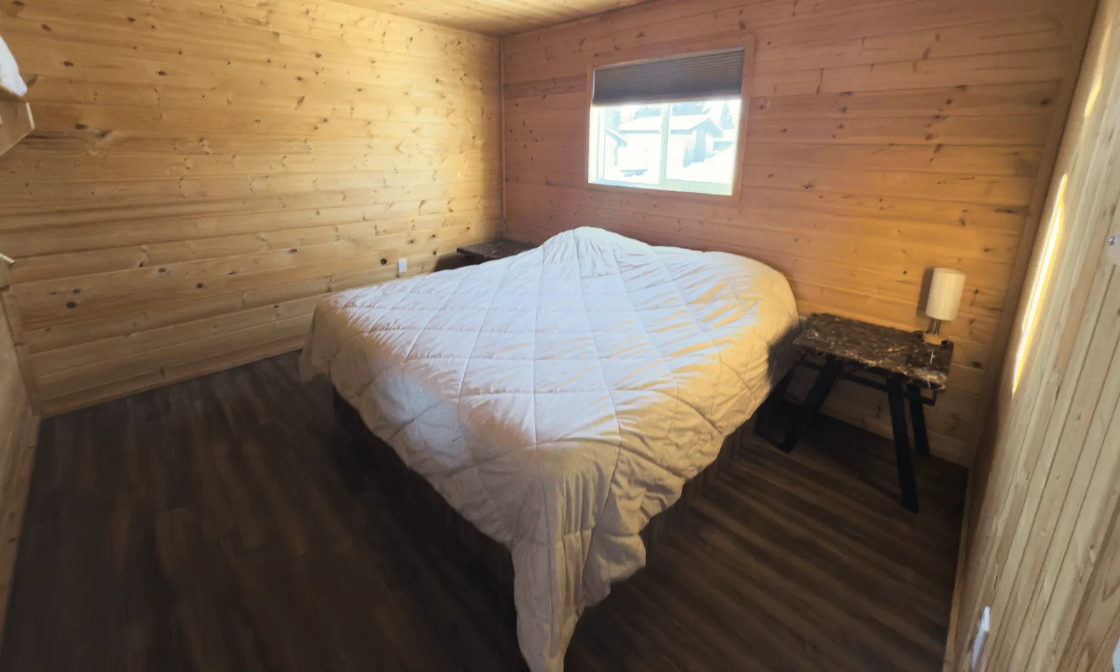 cabin bedroom interior with white comforter, wooden log wall paneling, and dark wood flooring.