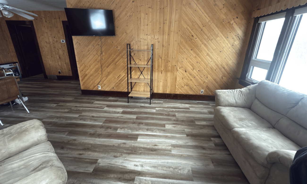 Compact cabin interior with wooden walls, gray flooring, a small mounted television.