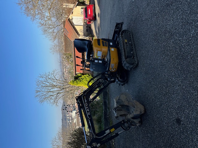 Man wearing safety glasses and gloves kneeling while installing flooring near wooden staircase with tools and toolbox nearby.