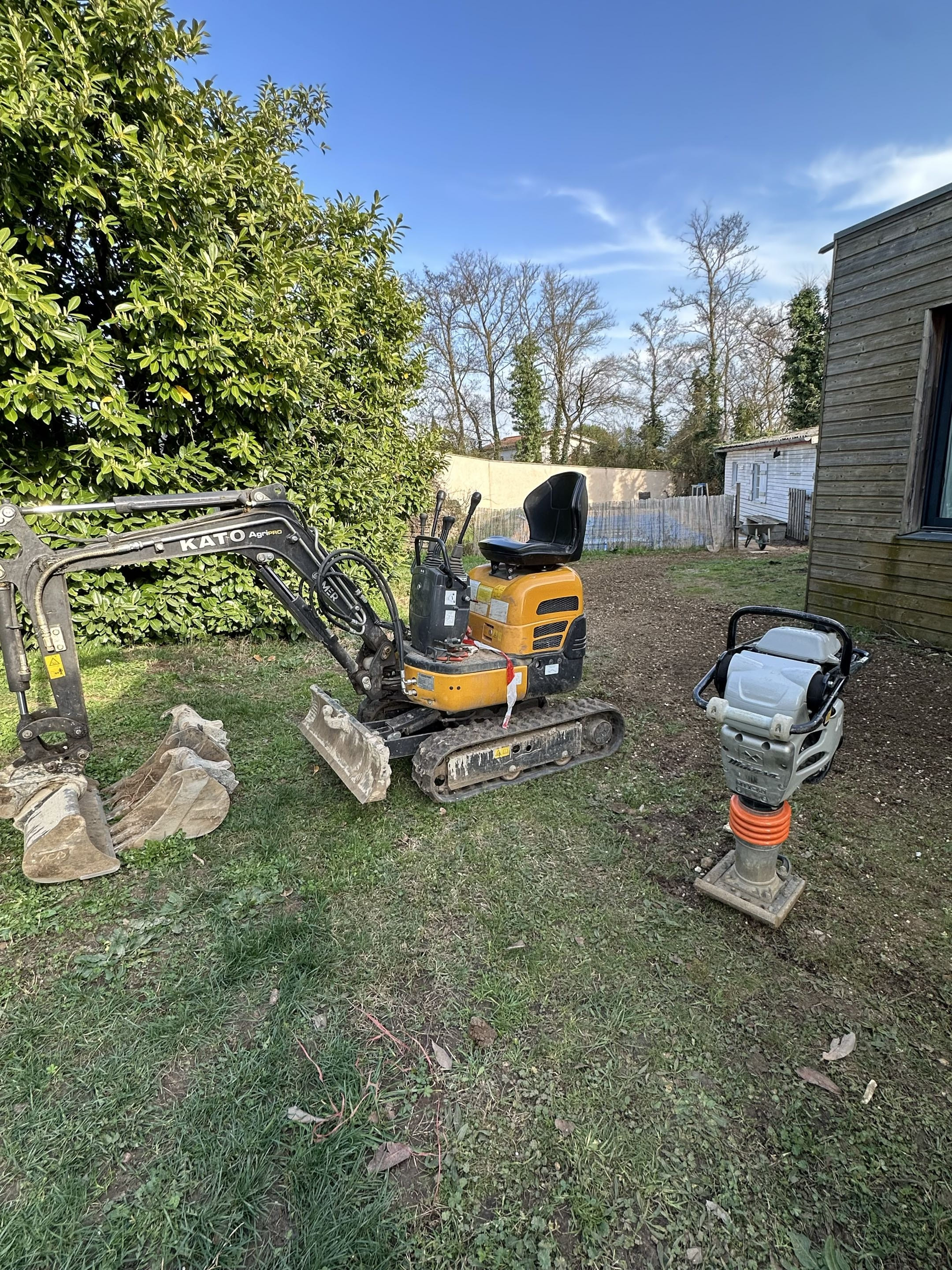 Small yellow and black excavator digging a hole in a grassy yard with a pile of dirt next to it.