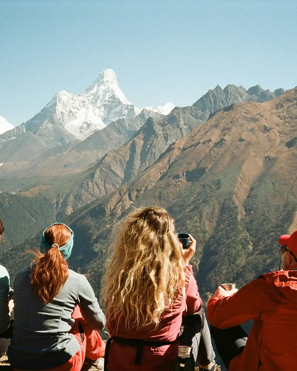 Travellers sitting on a mountain viewpoint with snow covered peaks in the background
