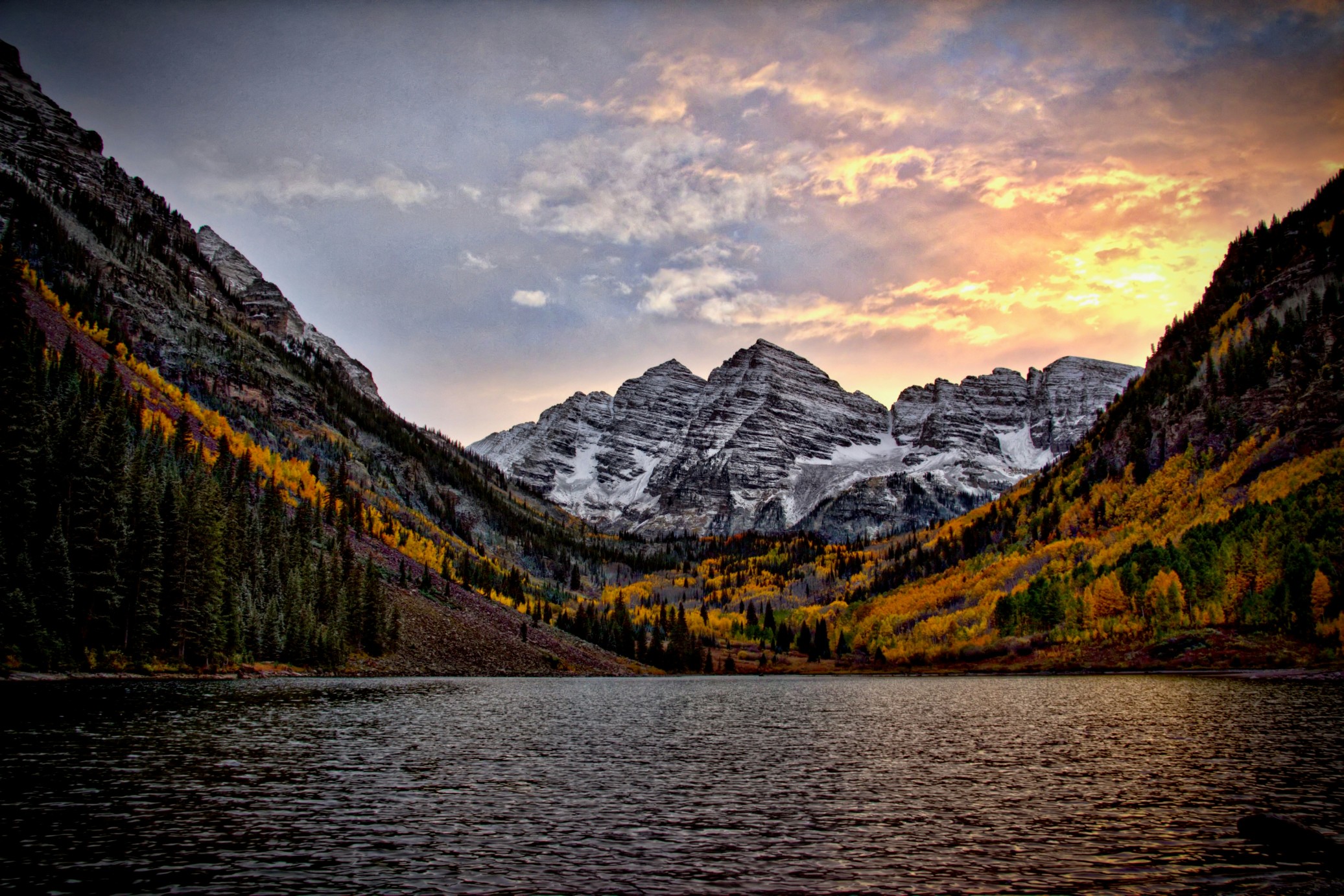 Snow-dusted Colorado mountains and golden autumn forest reflecting in a calm lake at dusk