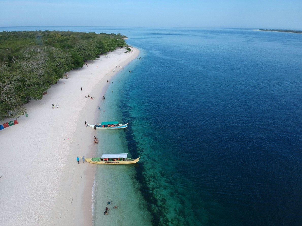 An aerial shot of traditional outrigger boats on a white sand beach with deep blue ocean water.