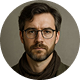 Portrait of a man with dark hair, beard, and glasses wearing a dark shirt against a neutral background.