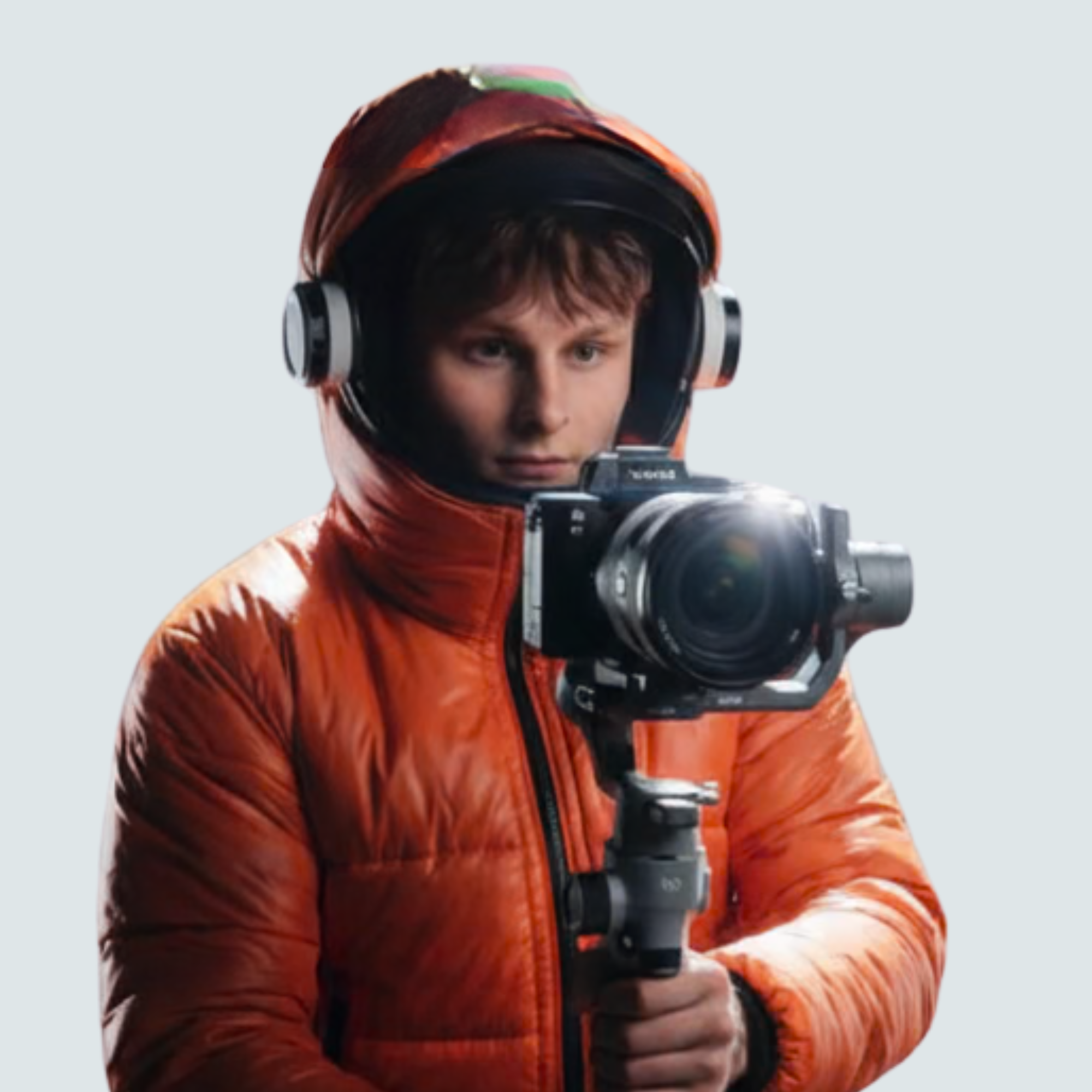 Person in orange hooded jacket using a camera mounted on a stabilizer.