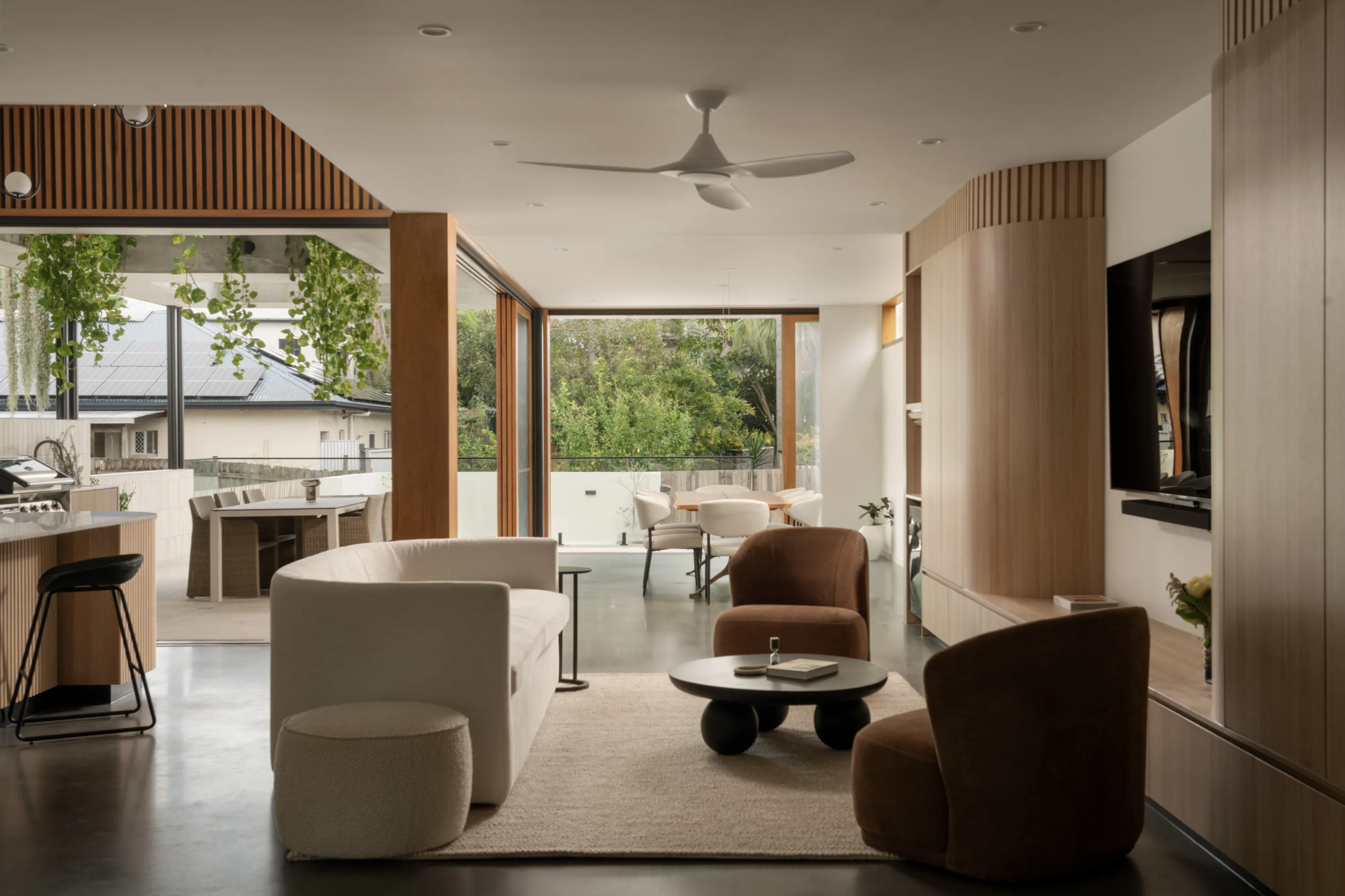 Modern living room with cream sofa, two brown chairs, round black coffee table, and large windows opening to patio.