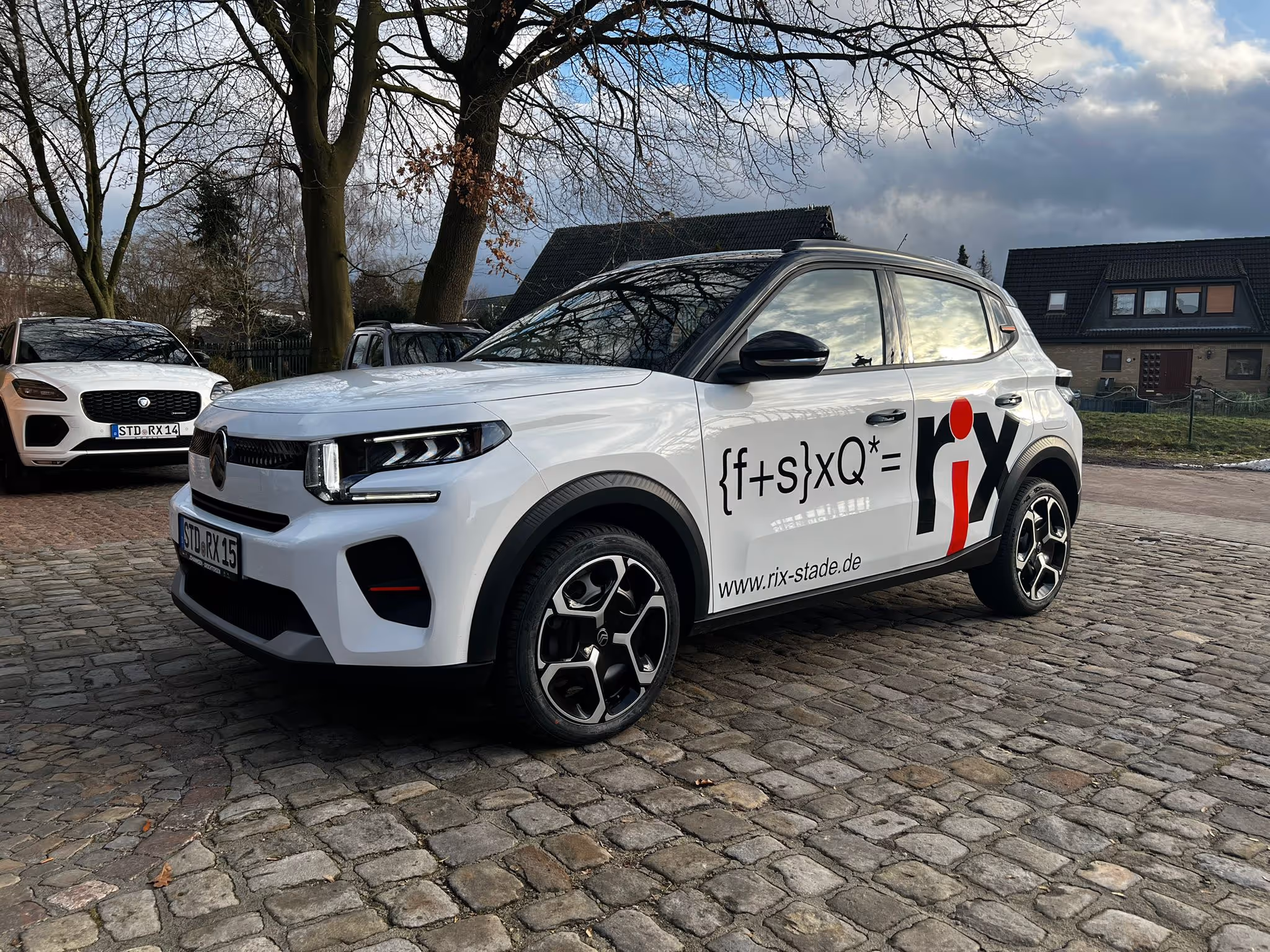 Weißer Citroën SUV mit schwarzem Dach parkt auf Kopfsteinpflaster, Fahrzeugbeschriftung zeigt Formel und www.rix-stade.de.