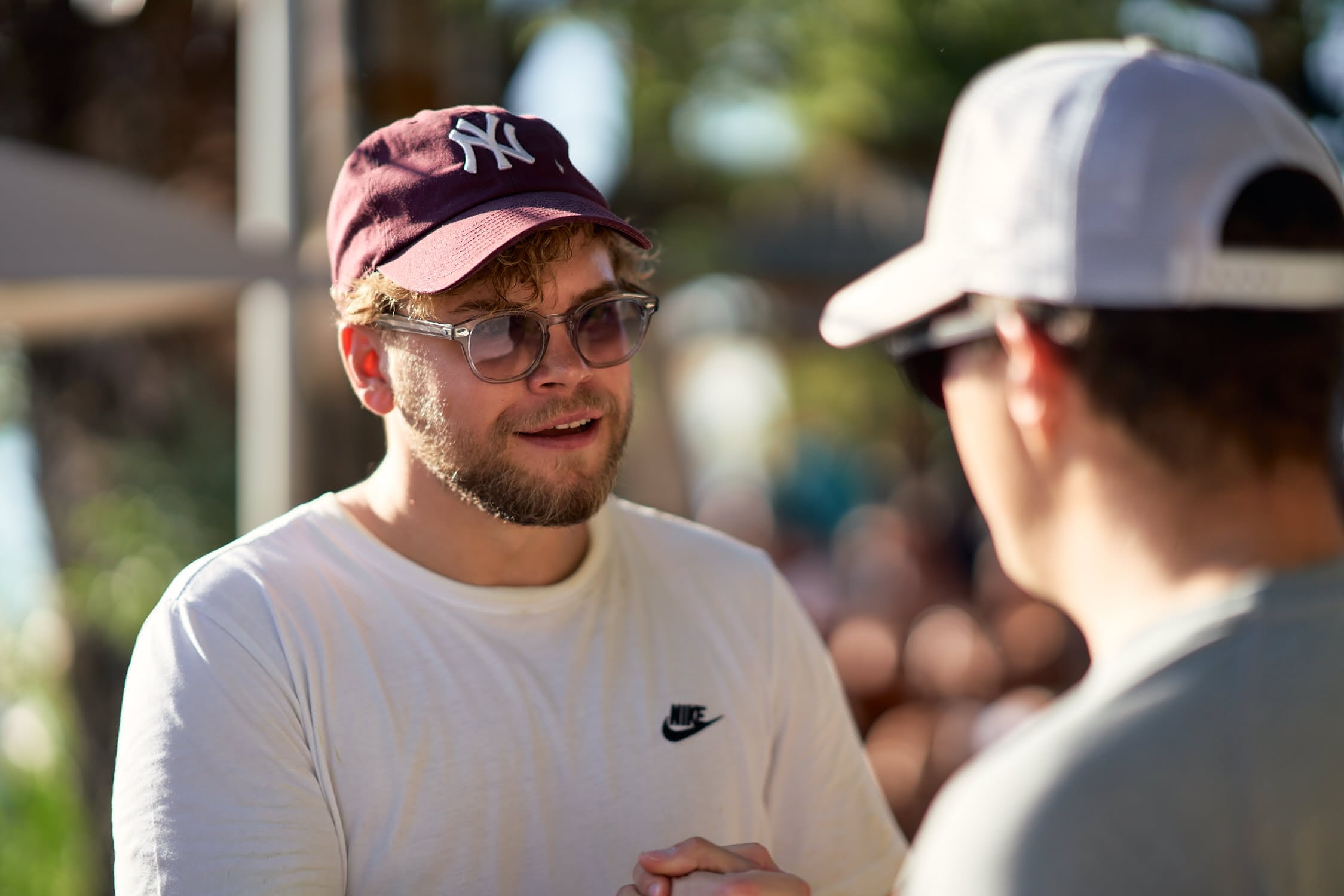 Zwei Männer mit Baseballkappen und Sonnenbrillen im Gespräch bei Sonnenlicht.