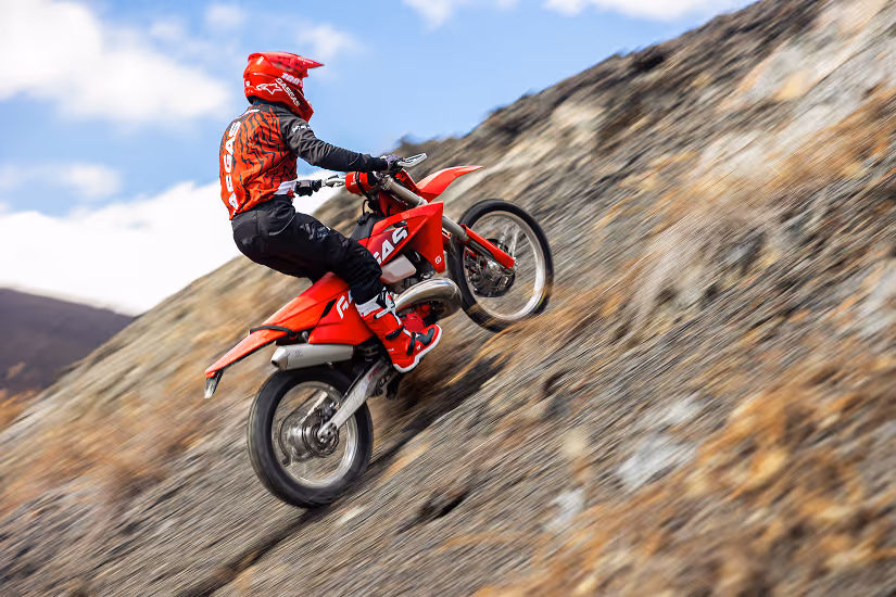 Motorcyclist in red gear riding a red enduro bike uphill on a Bulgarian rocky slope.