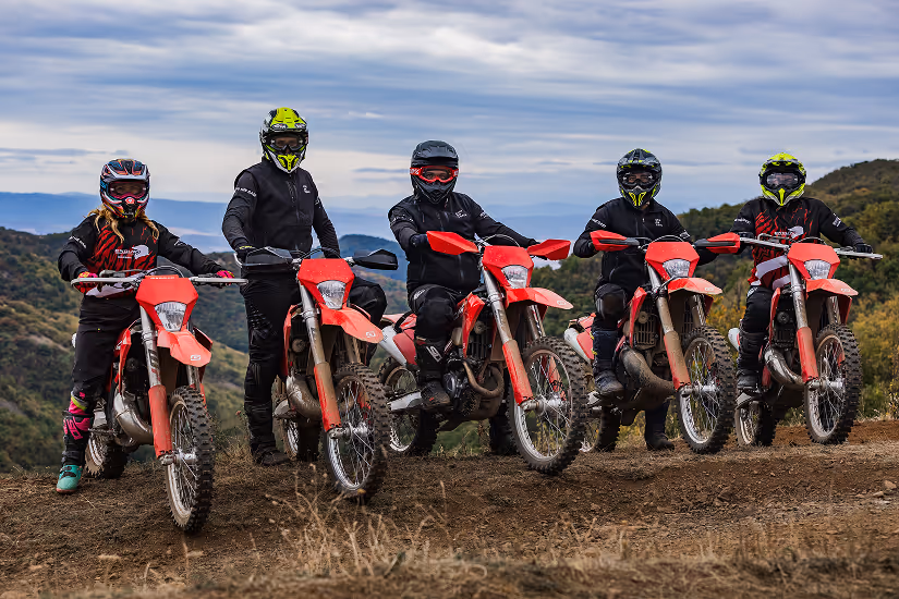 Five people wearing helmets and black riding gear on red enduro bikes outdoors with a mountainous, Bulgarian landscape in the background.