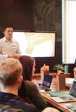 Three workers in orange uniforms cleaning a tree-lined street with leaves on the ground during autumn.