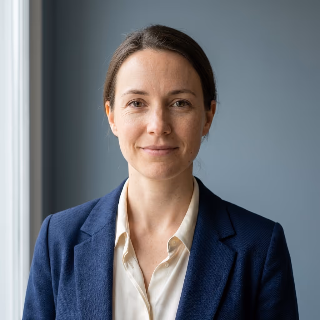 Professional woman with brown hair wearing a navy blazer and cream blouse, smiling gently against a gray background.
