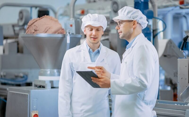 Zwei Qualitätsverantwortliche prüfen Produktionsdaten auf einem Tablet in einer Lebensmittelproduktion.
