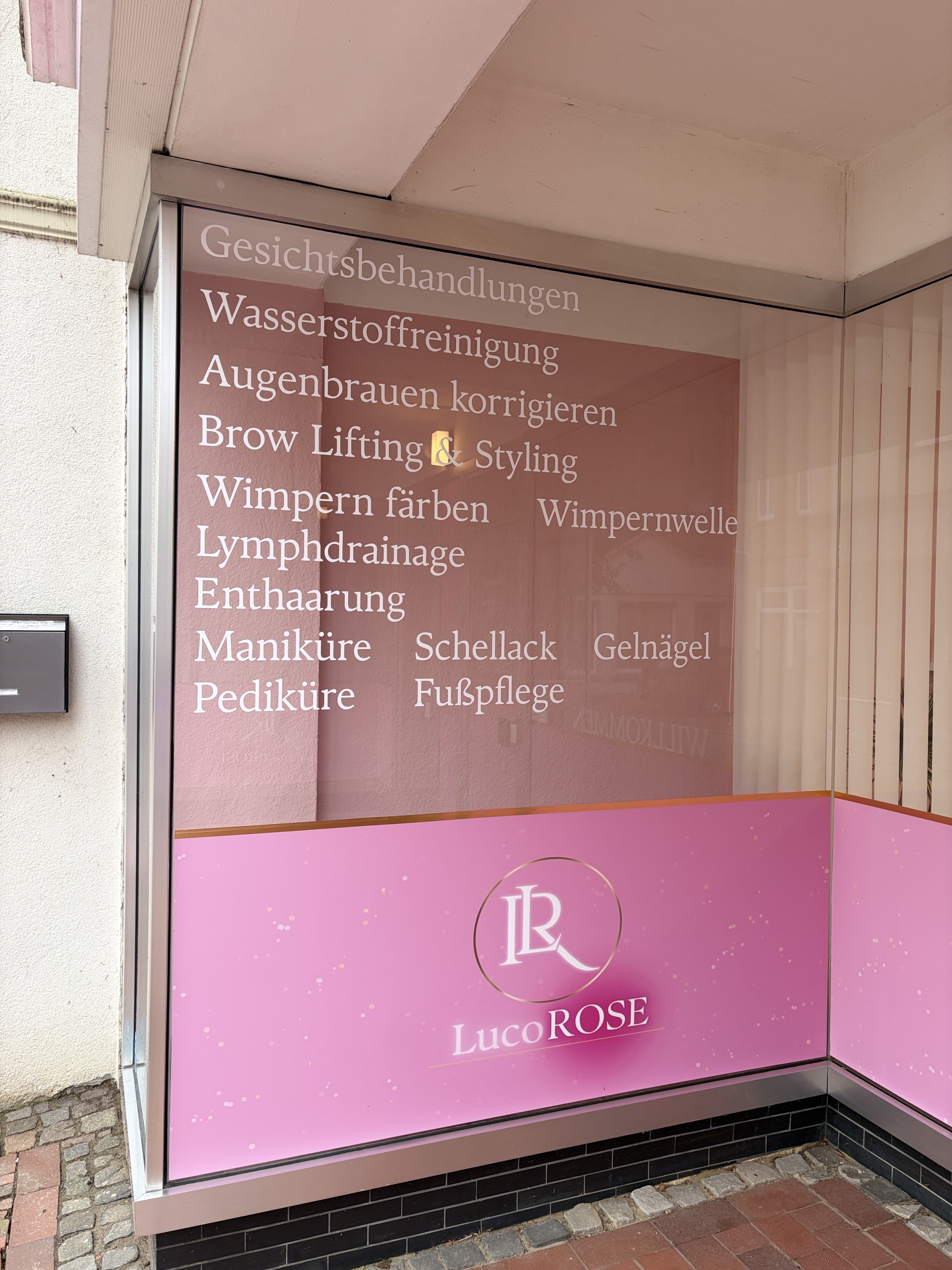 Schaufenster des LucoROSE Kosmetikstudios in Quakenbrück mit aufgelisteten Behandlungen wie Gesichtsbehandlungen, Wimpern und Maniküre
