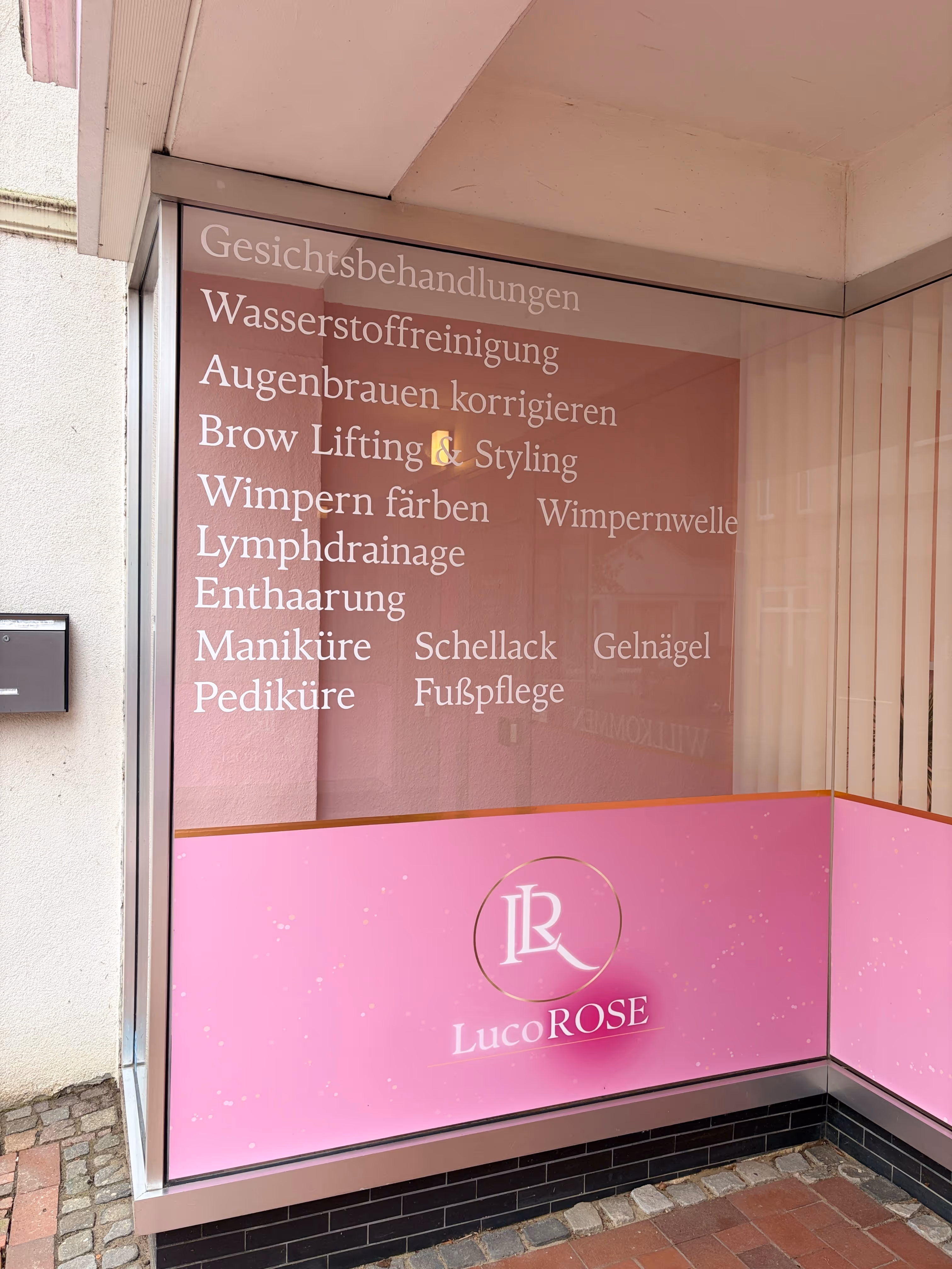 Schaufenster des LucoROSE Kosmetikstudios in Quakenbrück mit aufgelisteten Behandlungen wie Gesichtsbehandlungen, Wimpern und Maniküre