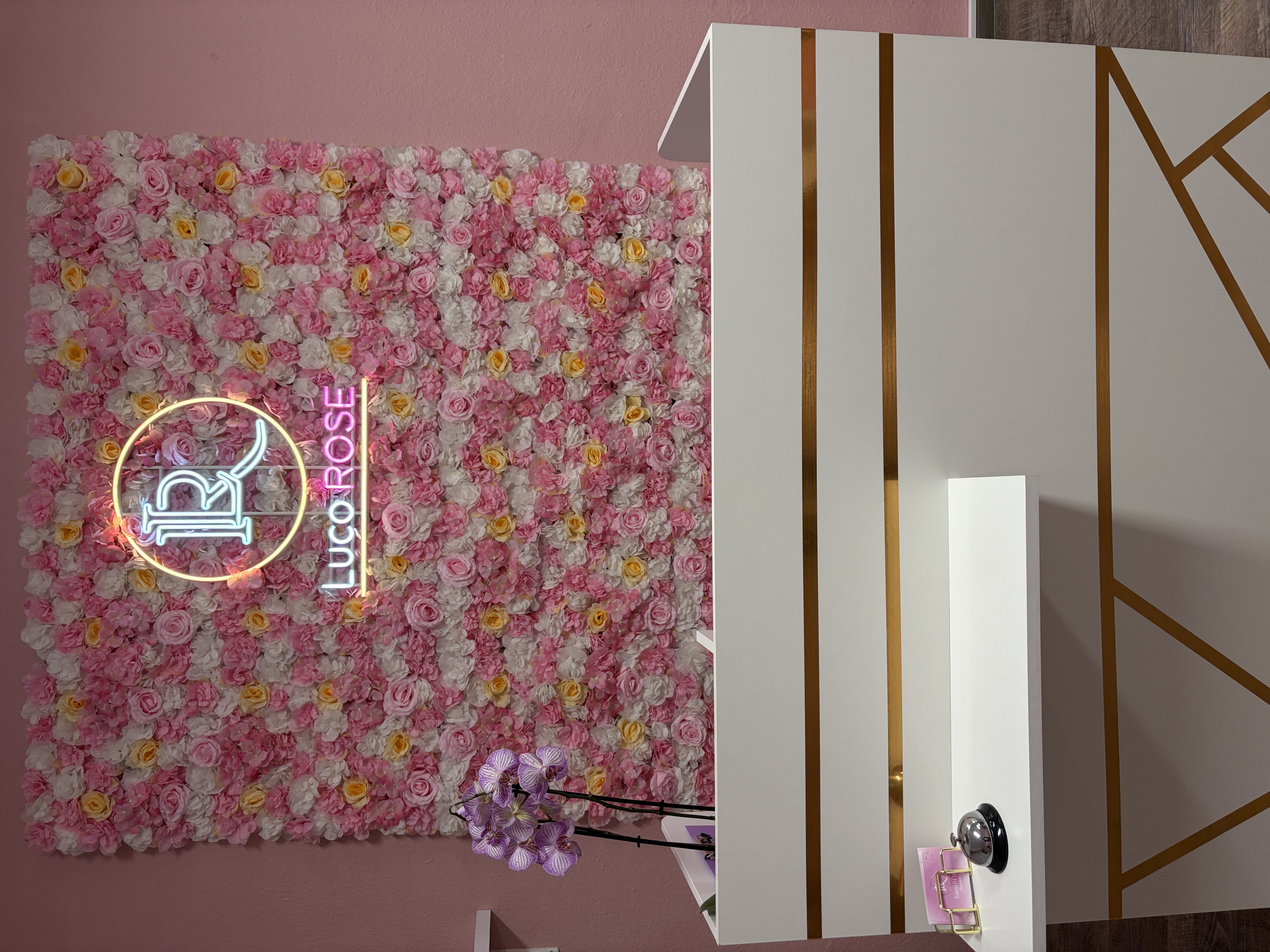 Empfangsbereich des LucoROSE Kosmetikstudios in Quakenbrück mit Blumenwand und beleuchtetem Logo