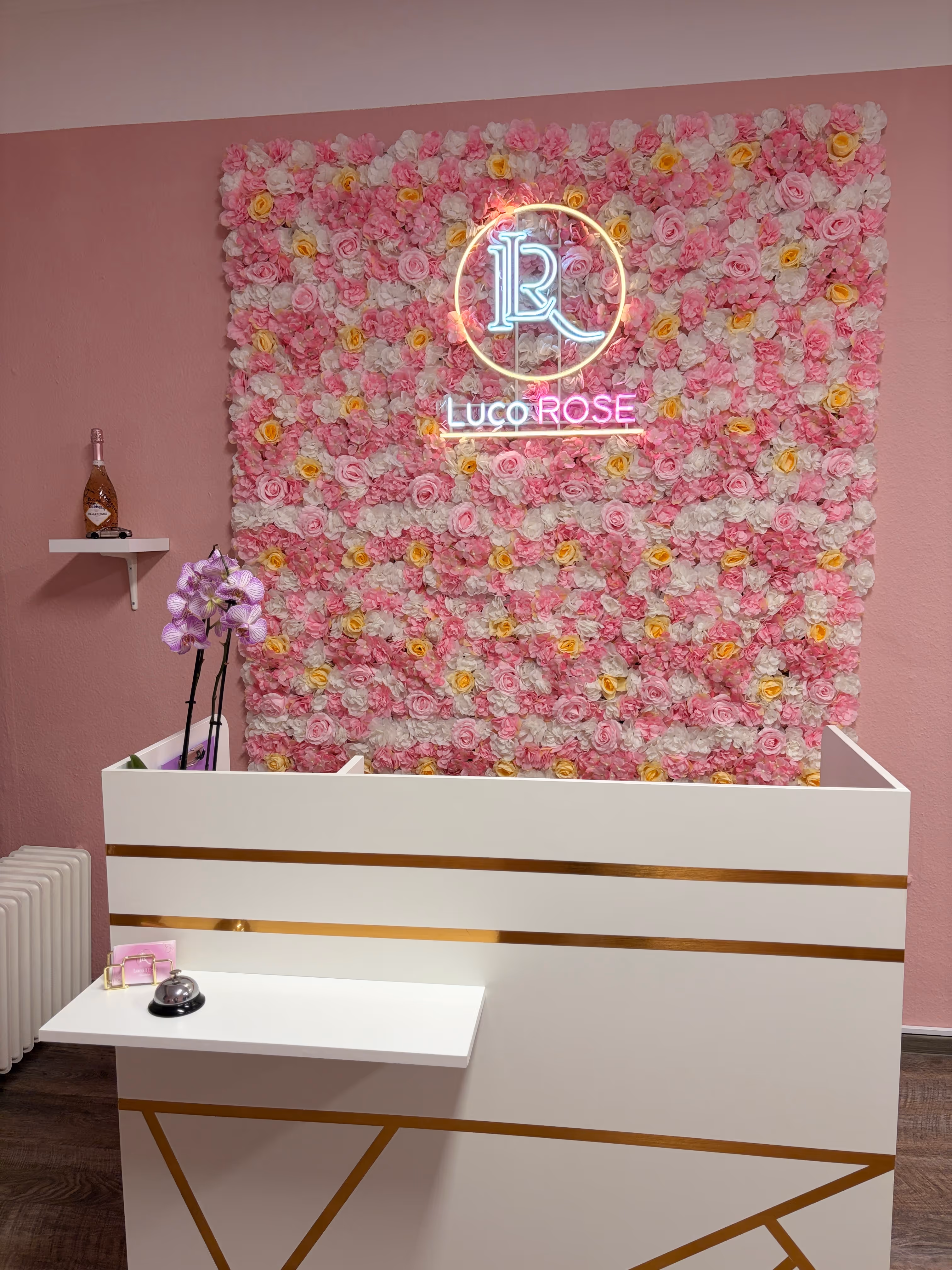Empfangsbereich des LucoROSE Kosmetikstudios in Quakenbrück mit Blumenwand und beleuchtetem Logo