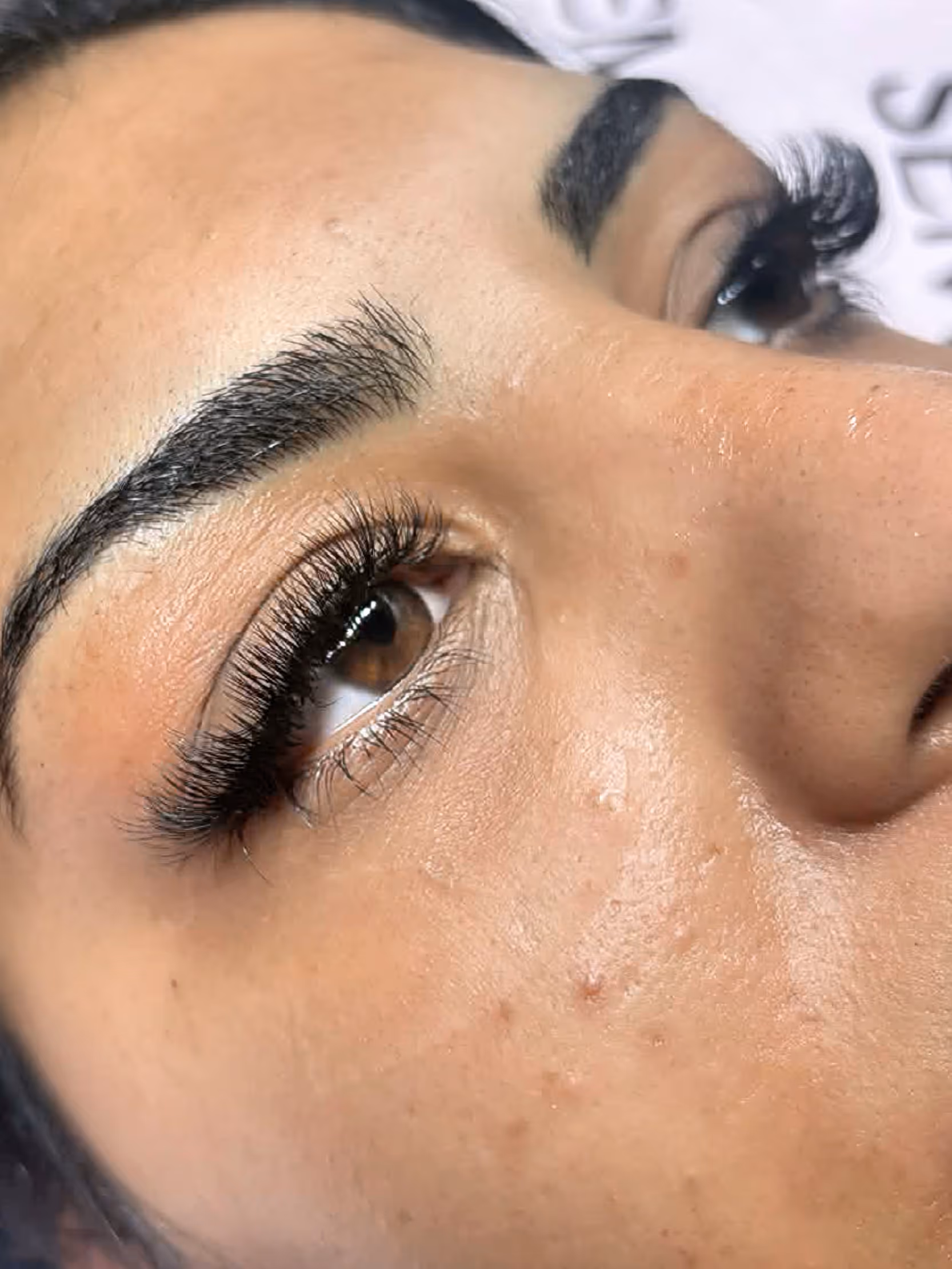 Close-up of a person's face focusing on eyes with long curled eyelashes and thick eyebrows, showing freckles on the skin.