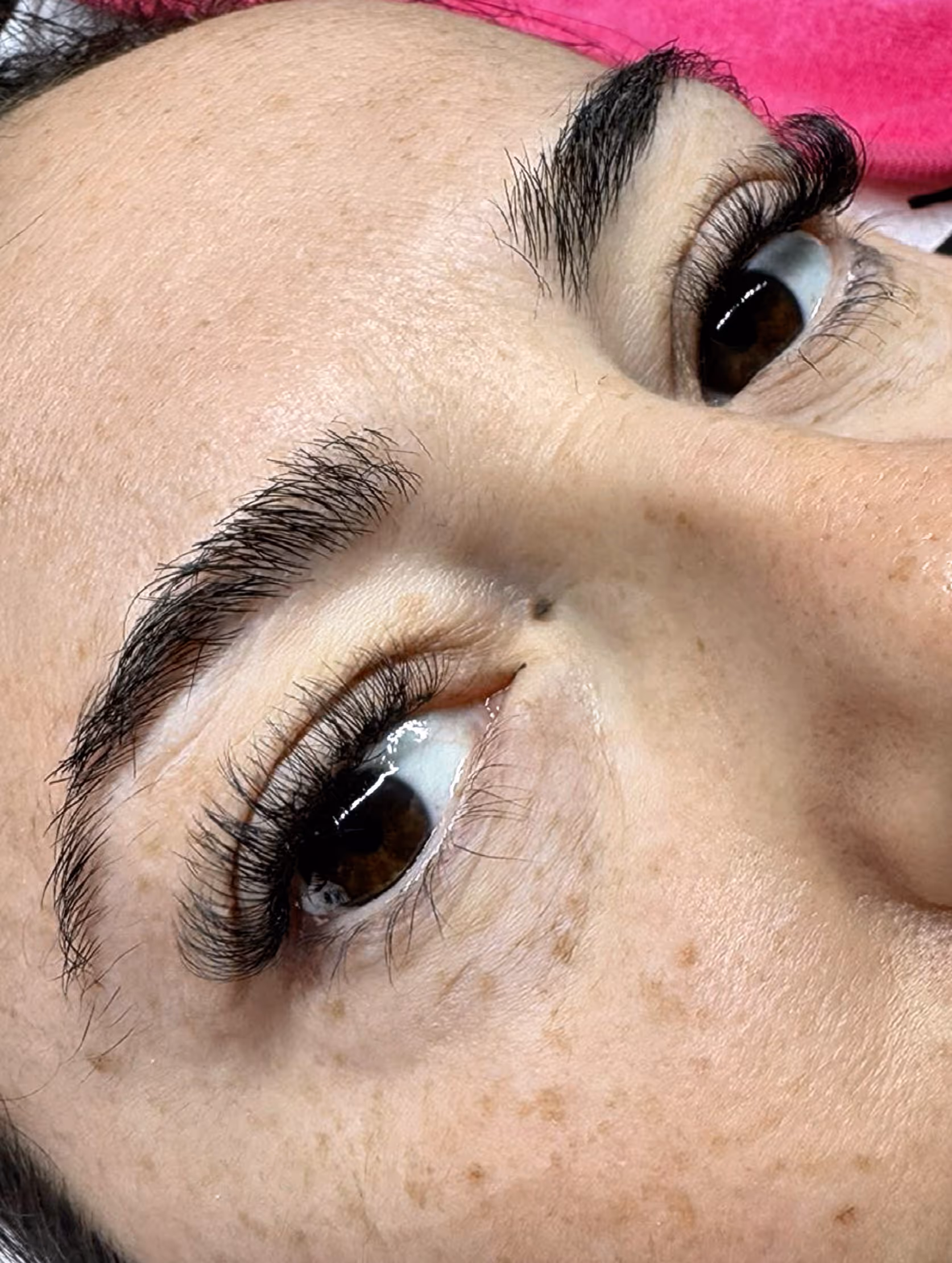 Close-up of a person's face focusing on eyes with long curled eyelashes and thick eyebrows, showing freckles on the skin.
