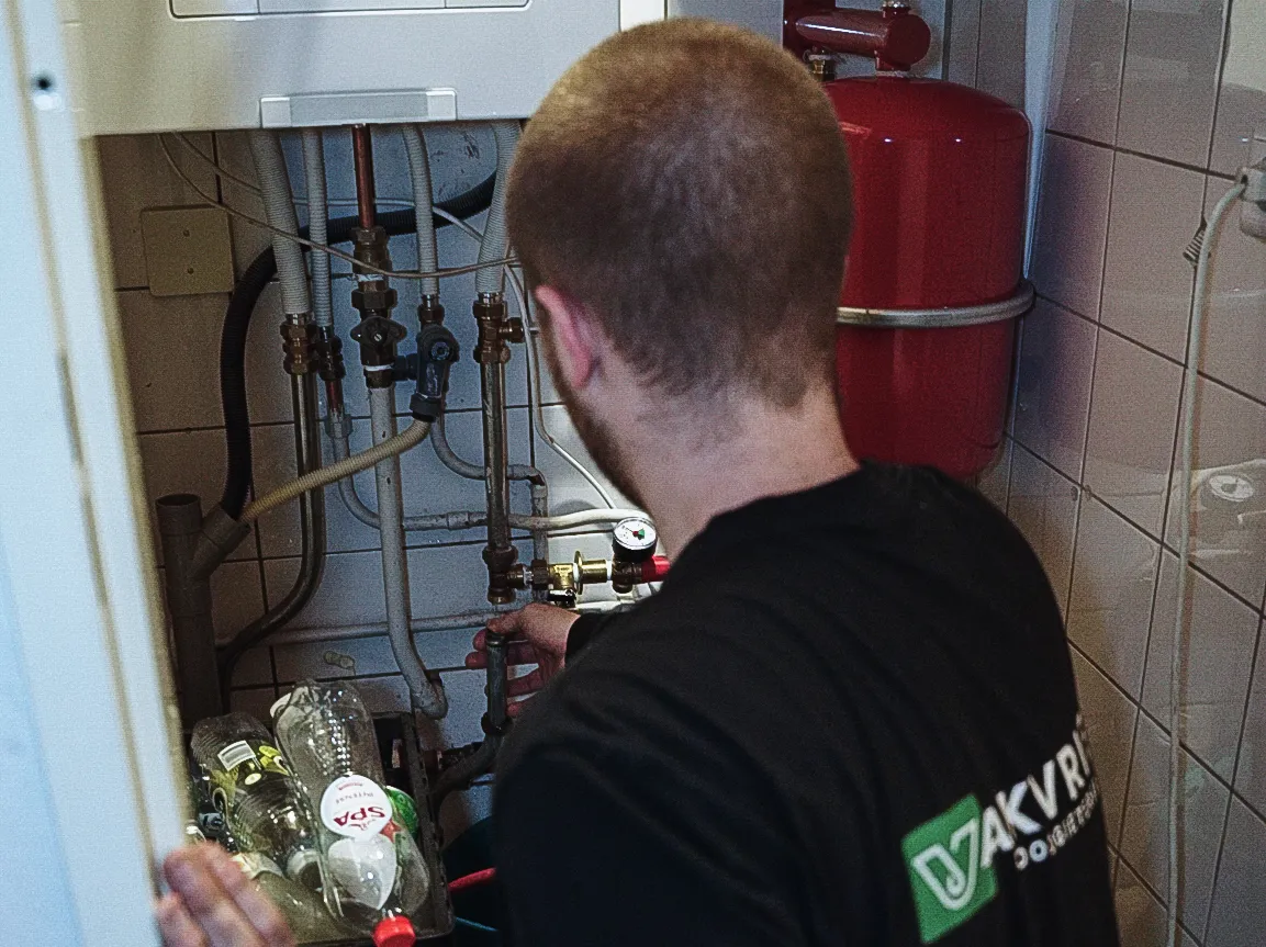 Man met zwart shirt werkt aan leidingen en kleppen in een technische kast met waterflessen erin.