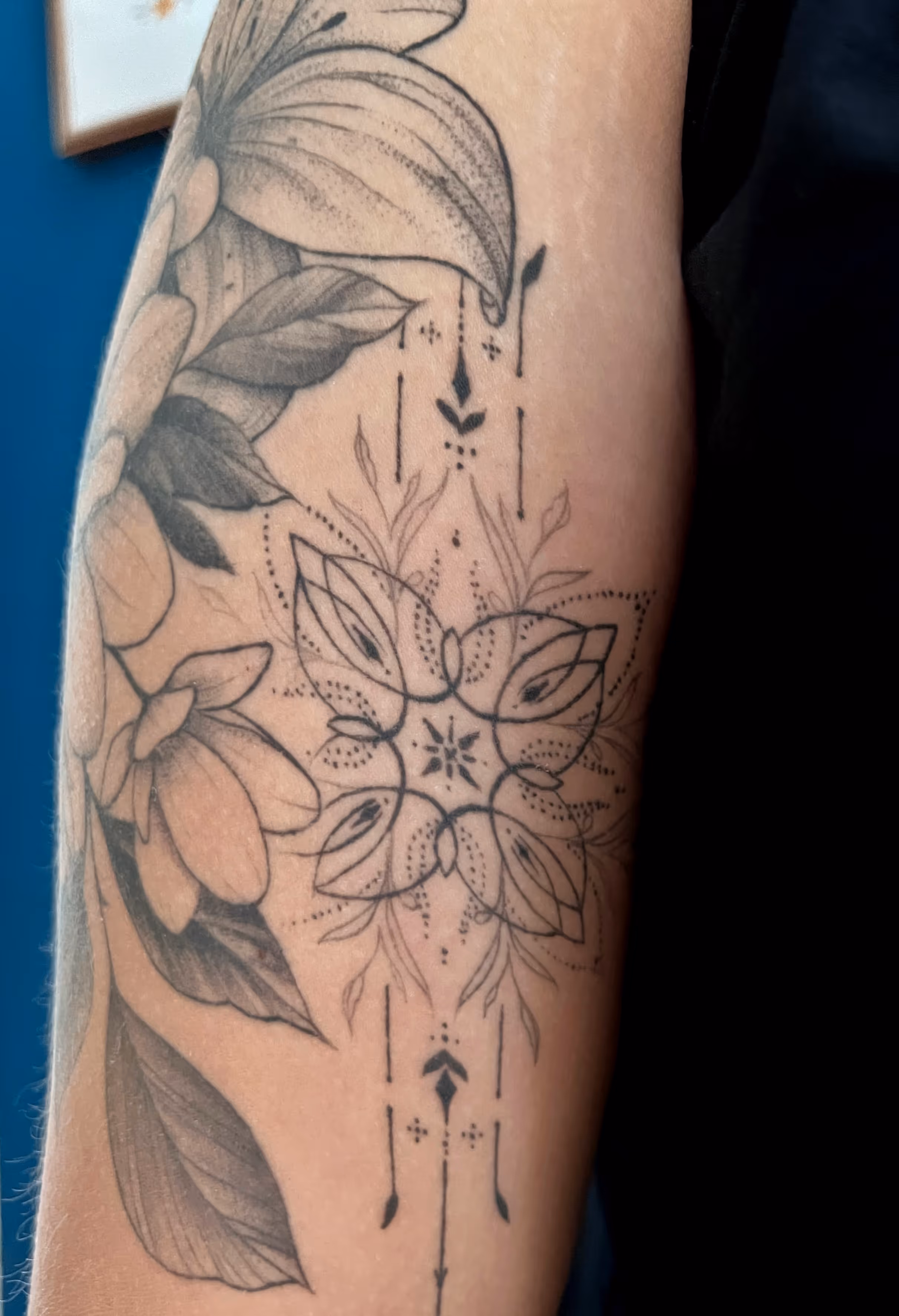 A forearm mandala tattoo next to a few flowers