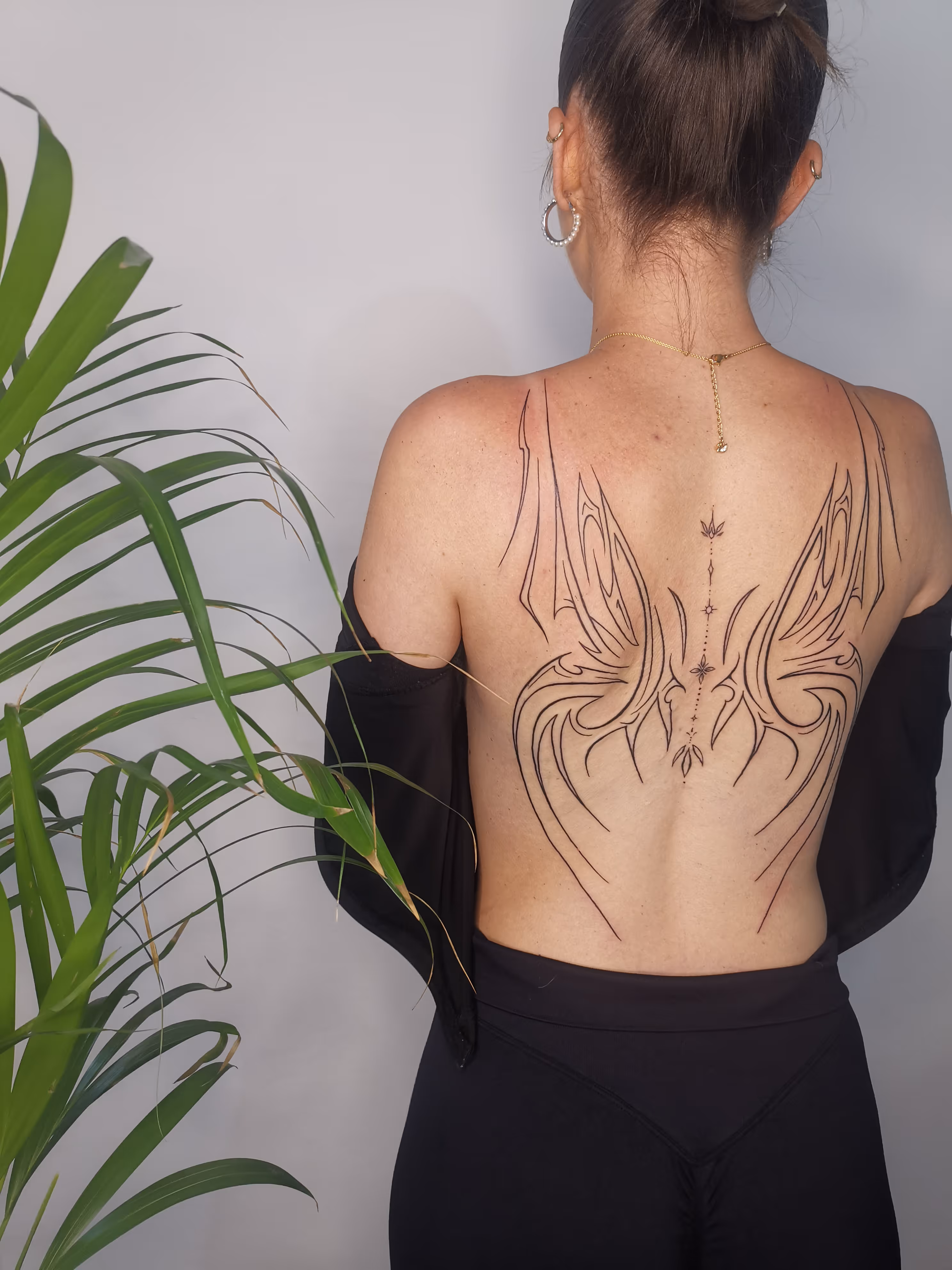A back piece tattoo using a fine line approach creating the shape of butterfly wings in the style of Ivy Tattoo