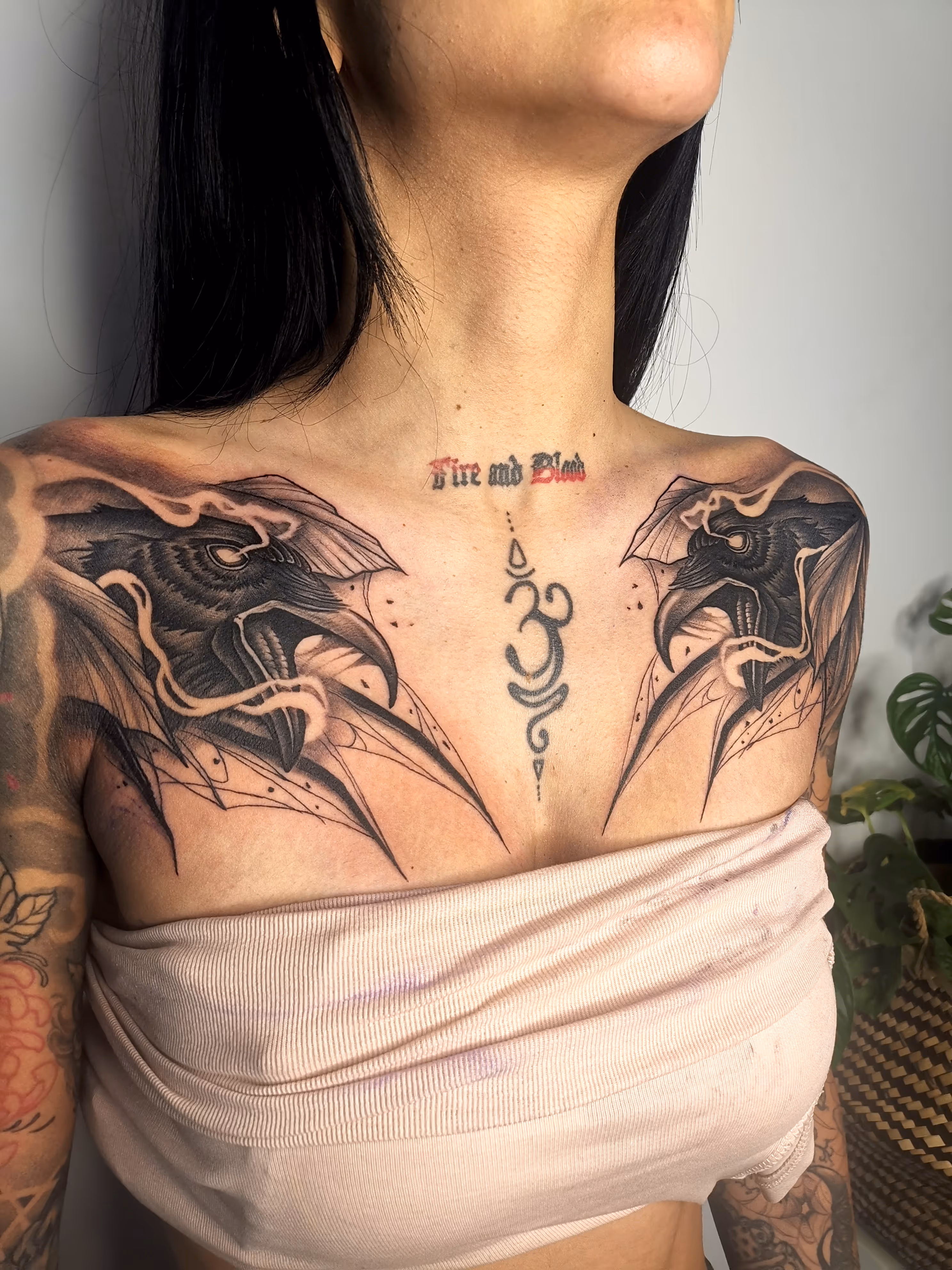 Picture of a chest piece tattoo featuring two cravens and a symbol in between that merges the sign for OM with the unalome