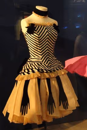 Robe vintage noire et blanche avec motif en zigzag et décorations de gants noirs suspendus sur la jupe jaune pâle.