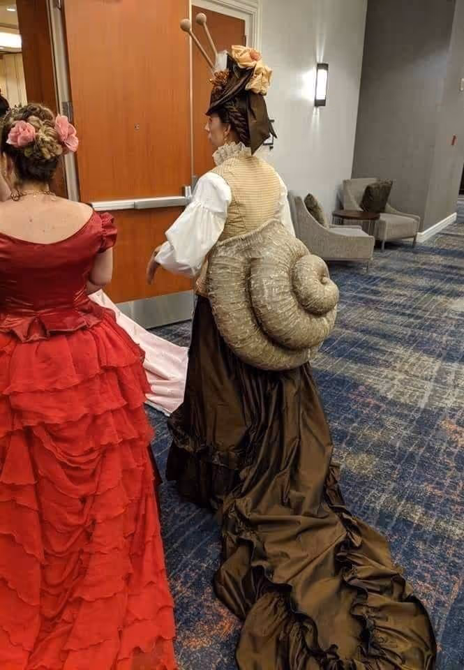 Deux personnes en costumes victoriens, dont une porte un déguisement d'escargot avec une grande coquille sur le dos.