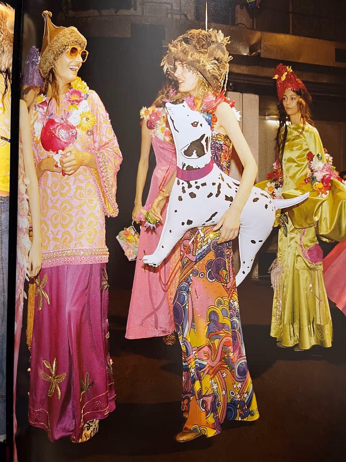 Quatre femmes en robes colorées et chapeaux originaux, dont une portant un chien gonflable blanc à taches noires.