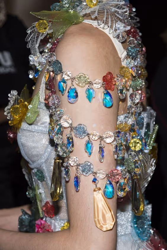 Bras orné de multiples bijoux colorés en plastique transparent en forme de fleurs et de gouttes, attachés à une robe blanche scintillante.