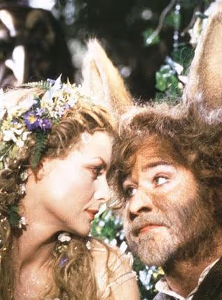 Une femme avec une couronne de fleurs regarde un homme aux oreilles d'âne dans un cadre forestier.