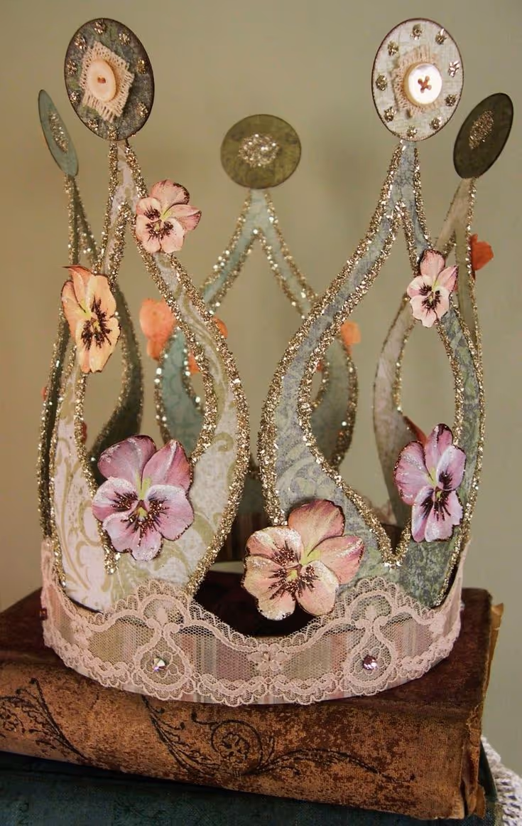 Couronne décorative ornée de fleurs roses, de paillettes dorées et de dentelle, posée sur des livres anciens.