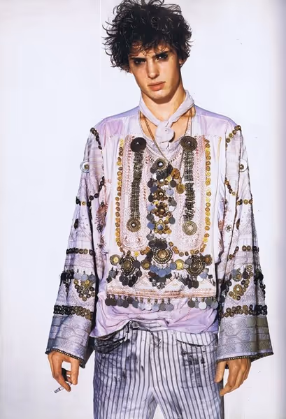 Mannequin défilant en robe fluide beige ornée de motifs floraux, avec de grandes ailes translucides et des fleurs dans les cheveux bouclés.