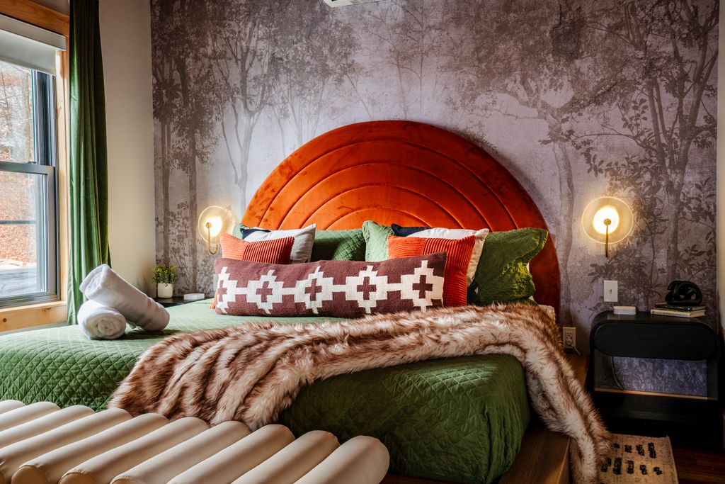 Bedroom with green quilted bedspread, rust-orange arched headboard, patterned pillows, faux fur throw, and bedside wall sconces.