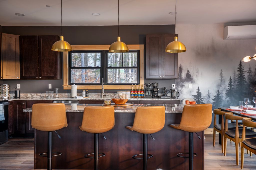 Modern kitchen with dark wood cabinets, marble countertop island, four tan leather bar stools, and three gold pendant lights, with a forest mural on the wall.