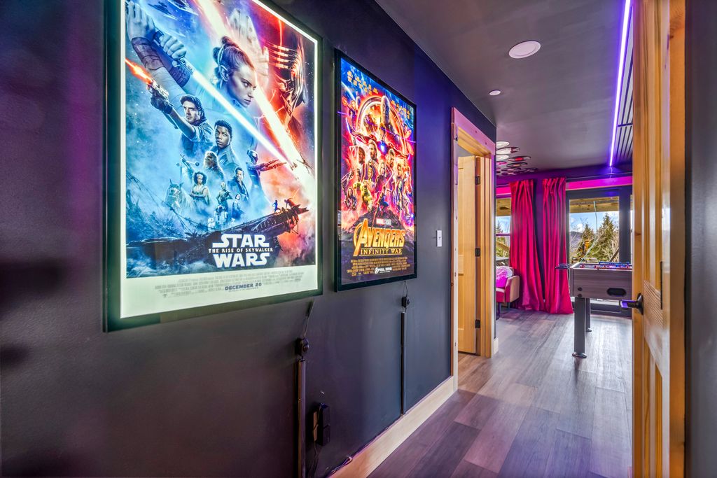 Hallway with illuminated Star Wars and Avengers movie posters on the dark wall, leading to a room with pink curtains and a foosball table.